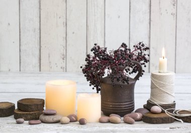 Rustic decoraton with candles, old reel and elderberries in a vase on a white wooden background clipart