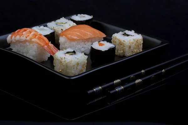 Sushi på fyrkantig platta över svart bakgrund — Stockfoto