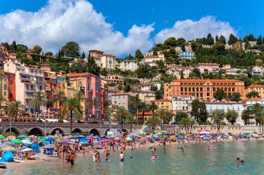 Menton, Fransa - 15 Ağustos 2014: Halk Plajı insanlar olarak arka planda Menton - Fransız Rivierası ve popüler turizm tesisi için onun bahçeleri ve yıllık limon festivaller ünlü küçük kasaba eski renkli evler.