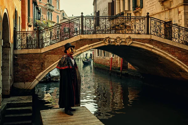 ヴェネツィア イタリア 2017 ブラック コスチューム マスクの中に有名な伝統的なカーニバルの開催毎年 月にイタリアのベニスで狭い運河の小さなヴェネツィアの橋の前でポーズに身を包んだ正体不明の男 — ストック写真
