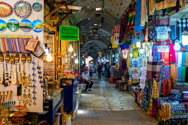 JERUSALEM, ISRAEL - JULY 16, 2017: Narrow street among shops and stalls with traditional souvenirs at famous bazaar - market in Old City of Jerusalem, famous place with tourists.