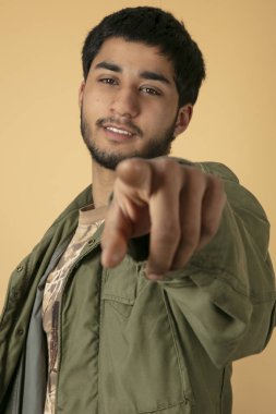 Genç adam bej renkli arka plan üzerinde parmakla işaret