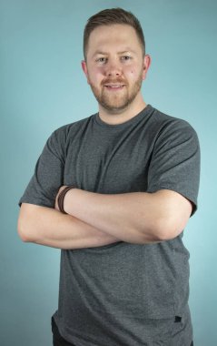 Sakallı rahat genç adam onun fotoğraf makinesi ile çapraz silah ver frontal stüdyo portre ikindilerde bakarak bir gri t-shirt