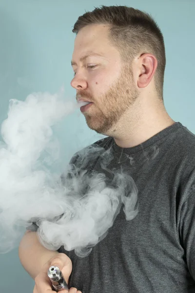 Buharlaştırıcı elinde tutan yüzünü engellemeyecek duman bulutu ile bir e-sigara sigara genç adam vaping
