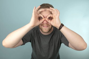 Genç adam bir stüdyo portre kameraya bakar gibi gözlerinin parmaklarıyla çevresinde bir gözlük veya gözlük jest yapma