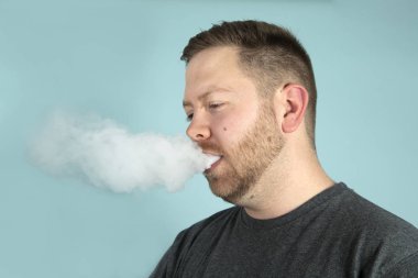 Vaping Studio gri bir arka plan yüzünde engellemeyecek duman bulutu ile genç adam