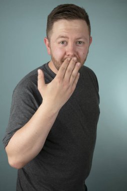 Öne doğru eğilen bir adam kameraya bakarken şaşkınlık, şaşkınlık ya da şaşkınlık içinde gri bir stüdyo arka planına bakıyordu.