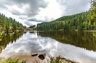 Sakin dağ gölü çevreleyen yansımaları ile yeşil ormanlar kayalık bir kıyı güneşli bir bulutlu günde görüntülendi