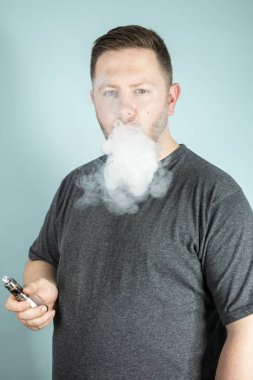 Buharlaştırıcı elinde tutan yüzünü engellemeyecek duman bulutu ile bir e-sigara sigara genç adam vaping