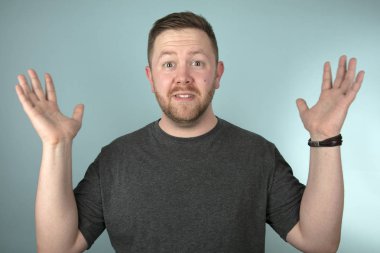 Öne doğru eğilen bir adam kameraya bakarken şaşkınlık, şaşkınlık ya da şaşkınlık içinde gri bir stüdyo arka planına bakıyordu.