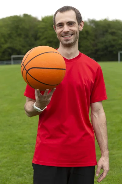 Freundlicher junger Mann hält einen Basketball in der Hand — Stockfoto