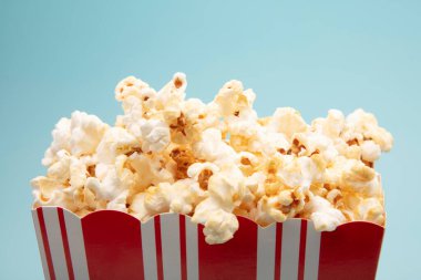 Parlak mavi arka planda tuzlanmış Pocorn ile dolu büyük kağıt bardak.