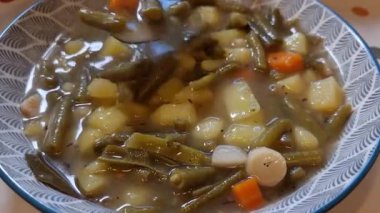 Metal kaşık yeşil fasulye çorbasını patates, havuç ve baharatla karıştırıyor.