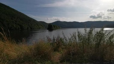 Huzurlu deniz gölü etrafındaki tepeleri ve gökyüzünü yansıtıyor.