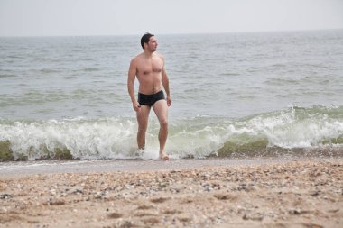 Şortlu genç adam seçici bir odak ile denizden çıkıyor.