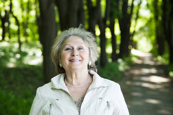 portrait of smiling senior aged woman outdoors in forest with copy space