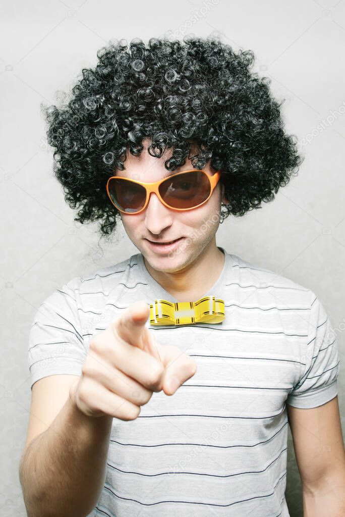 funny guy in afro curly wig with eyeglasses and ribbon bowtie pointing with his finger