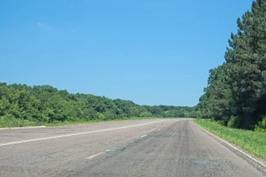 Ağaçlı ve bulutsuz mavi gökyüzü ve kopya alanı olan boş kırsal karayolu.