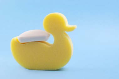 Açık mavi arkaplanda sabun taşıyan sarı ördek süngeri