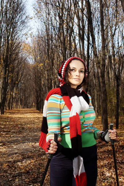 Closeup of young woman with Nordic walking poles in autumn forest alley with selective focus