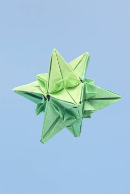 Soyut şekilli yeşil kağıt origamisinin mavi arkaplana karşı seçici bir odak ile izole edilmesi