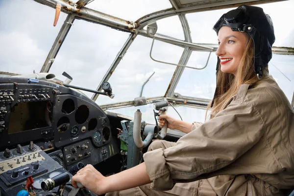 Beautiful woman pilot in a helmet and pilot suit sits in the cockpit of a small propeller plane