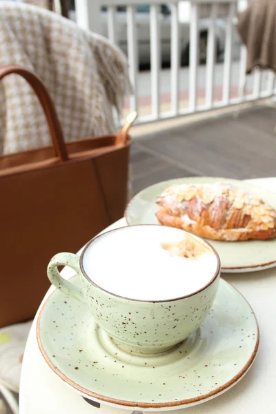 一杯拿铁咖啡和一个在桌上的夏日咖啡馆里的羊角面包 — 图库照片