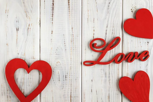 Wooden letters love and red hearts on a white wooden background. Background or postcard