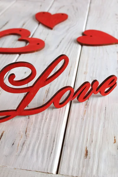 Wooden letters love and red hearts on a white wooden background. Background or postcard