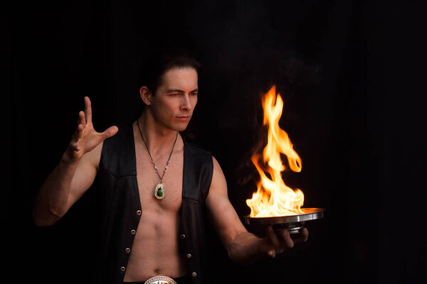 The magician controls the fire in a black leather waistcoat on a black background