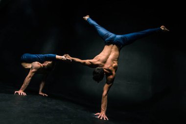 Erkek akrobatik duo karmaşık dengeyi karanlık bir arka plan üzerinde gerçekleştirir..