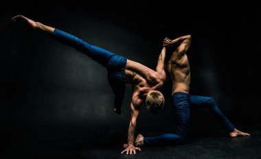 Erkek akrobatik duo karmaşık dengeyi karanlık bir arka plan üzerinde gerçekleştirir..