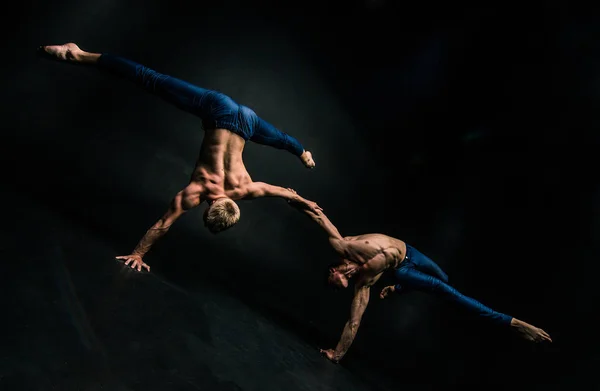 Male acrobatic duo performs a complicated balancing act on a dark background.