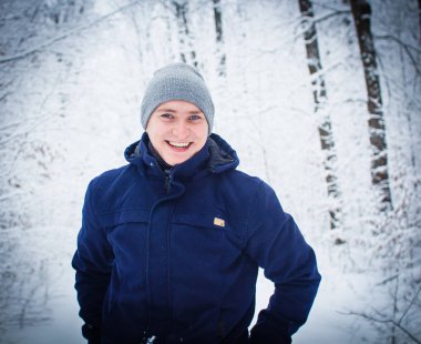 Sıcak ceket karlı ormanı'nın arka plan bulanık kameraya gülümseyen yakışıklı delikanlı.