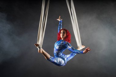 athletic sexy aerial circus artist with redhead in blue costume dancing in the air with balance clipart