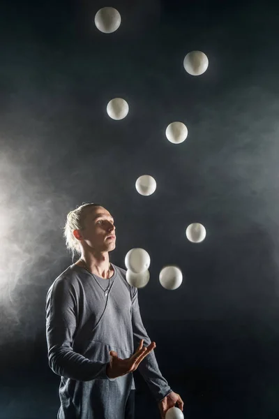 Блондин жонглер с белыми шарами на черном фоне — стоковое фото