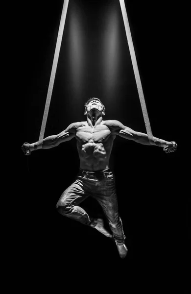 Artista de circo muscular en las correas aéreas haciendo cruz con fuertes músculos sobre fondo negro — Foto de Stock
