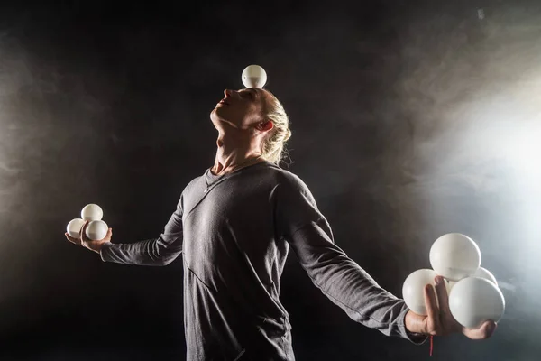 Блондин жонглер зберігає баланс білих кульок на чорному тлі — стокове фото