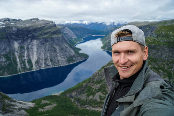 Young traveller taking selfie on the top with Beautiful fjord on background in Norway