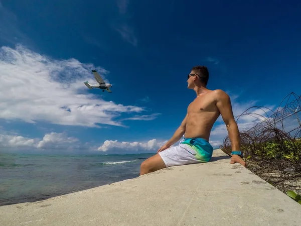 Un uomo muscoloso seduto di fronte all'aereo di atterraggio sulla costa di Montego Bay. Giamaica — Foto Stock