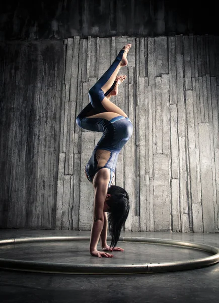 Young female Acrobat Standing on Hand over gray background in photo studio. Flexible Woman Circus Gymnast, Gymnastics Handstand.