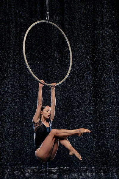 Vackra kvinnliga acrobat hängande med graciösa pose på aerial hoop under regn på svart bakgrund — Stockfoto