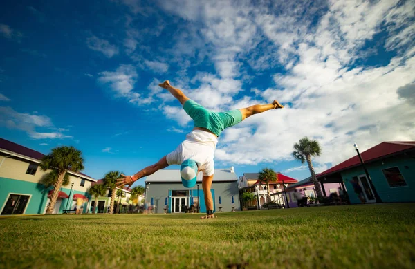 Young man standing on one hand on the grass with blue sky on background — ストック写真