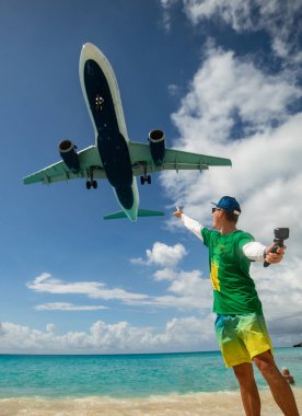 Arka planda uçan uçak ve plajla selfie çeken adam. Maho plajı. Mutlu tatil ve seyahat konsepti