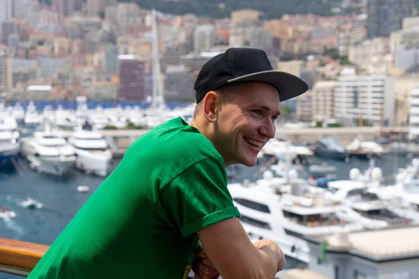 Joven hombre guapo sonriendo en el barco con veleros borrosos y barcos en el fondo. Monte Carlo, Mónaco — Foto de Stock