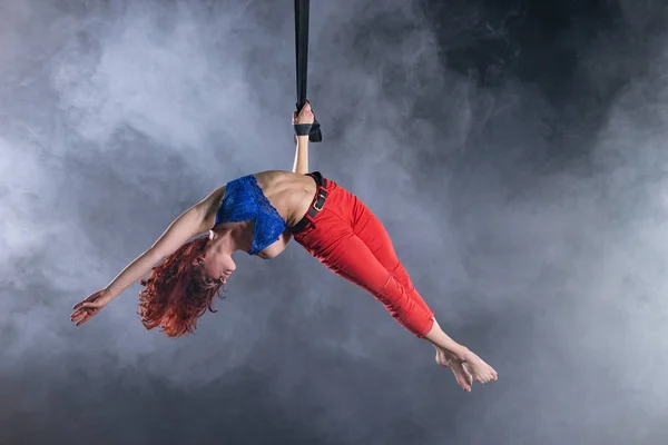 Жіночий спортивний, сексуальний і гнучкий артист повітряного цирку з рудим на повітряних ремінцях на чорному тлі — стокове фото