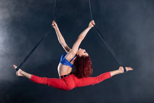 Weibliche athletische, sexy und flexible Zirkusartistin mit Rotschopf auf Antennenriemen auf schwarzem Hintergrund — Stockfoto