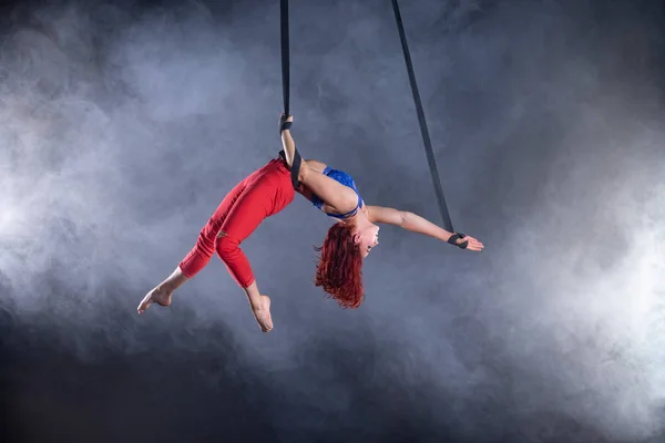 Жіночий спортивний, сексуальний і гнучкий артист повітряного цирку з рудим на повітряних ремінцях на чорному тлі — стокове фото
