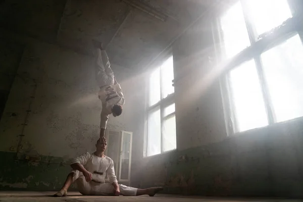 Manliga Duo gör akrobatiska tricks bär kostym av vansinniga människor i övergivna rum med solstrålar från Windows — Stockfoto