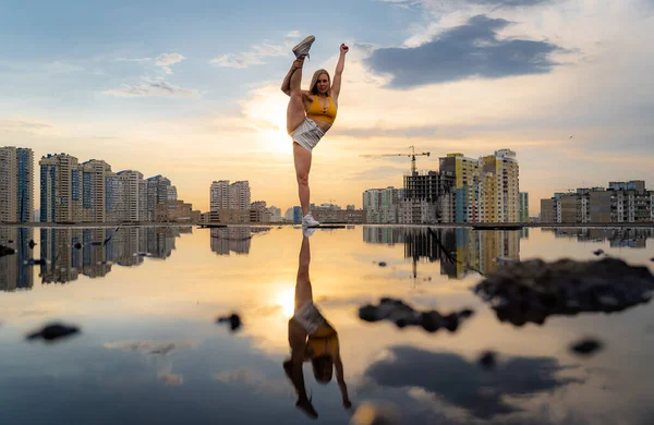 Gimnasta femenina flexible haciendo truco con reflejo en el agua durante la dramática puesta del sol — Foto de Stock